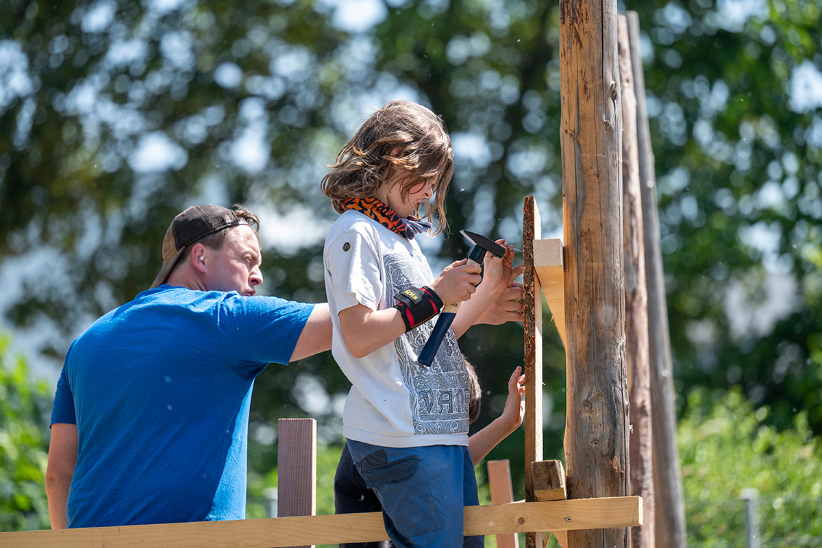 Kinder und Anleiter nageln Bretter an eine Hütte