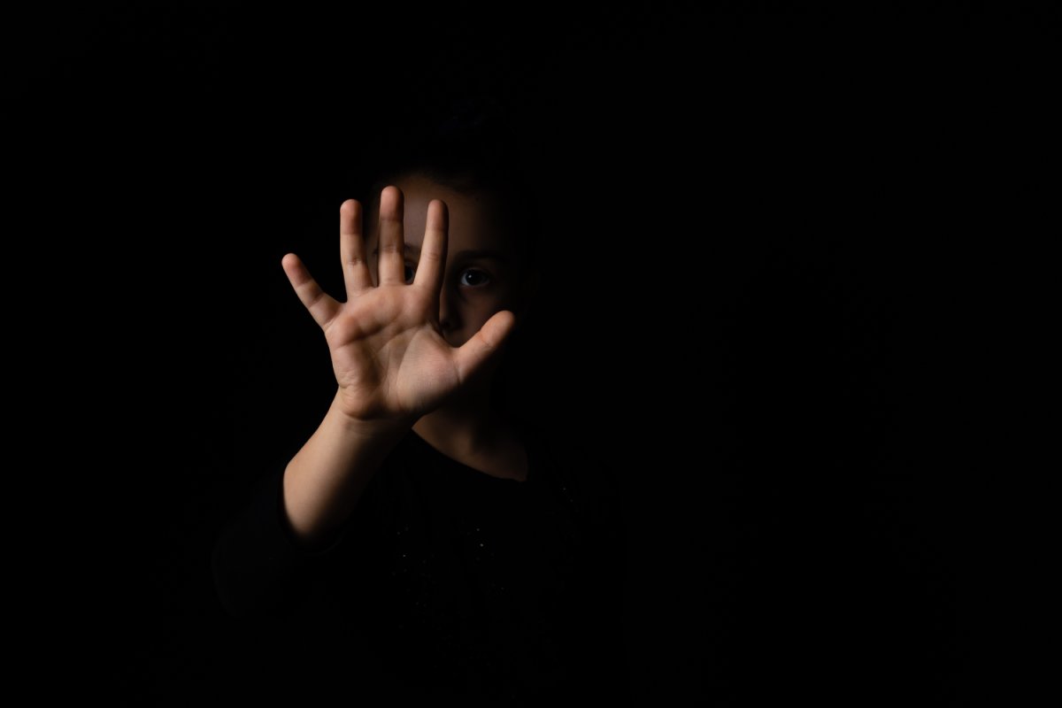 Kleines Mädchen mit erhobener Hand, das eine Stoppschildgeste auf schwarzem Hintergrund macht.