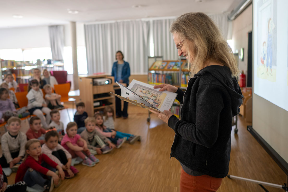 Eine Frau liest einer Gruppe von Kindern in einer Bibliothek aus einem Buch vor.