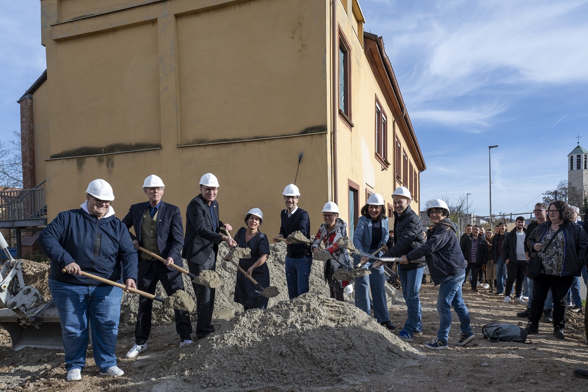 Viele Menschen mit einem Spaten und einem Helm werfen Sand in Richtung der Kamera