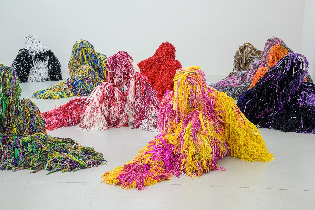 Ausstellungsansicht mit  kauernden Figuren in bunten Tarnanzügen von Yongkuk Ko