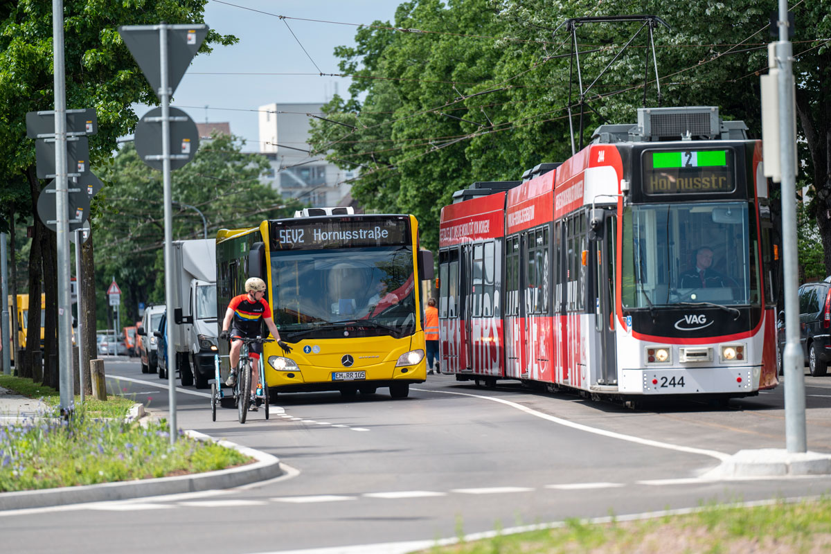 Fahrradfarer, Bus und Bahn stehen an einer Ampel