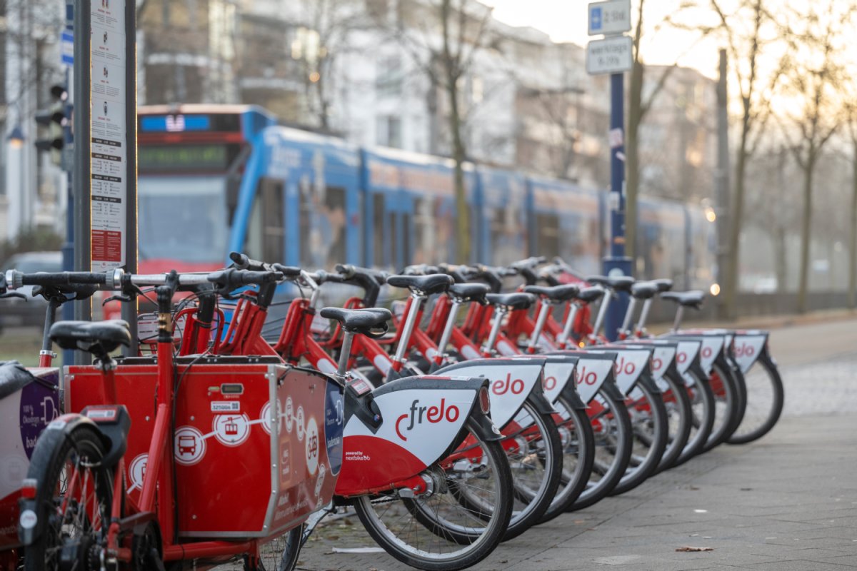 Eine Reihe an Leih-Fahrrädern, dahinter eine Straßenbahn.