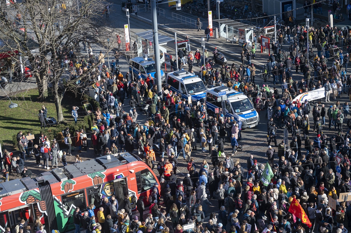 Viele Menschen haben sich versammelt und blockieren die Straßenbahn. Mittendrin stehen auch drei Polizeiwagen.
