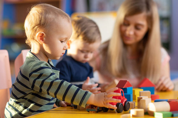 Zwei Kita-Kinder und eine Betreuerin spielen mit Bauklötzen