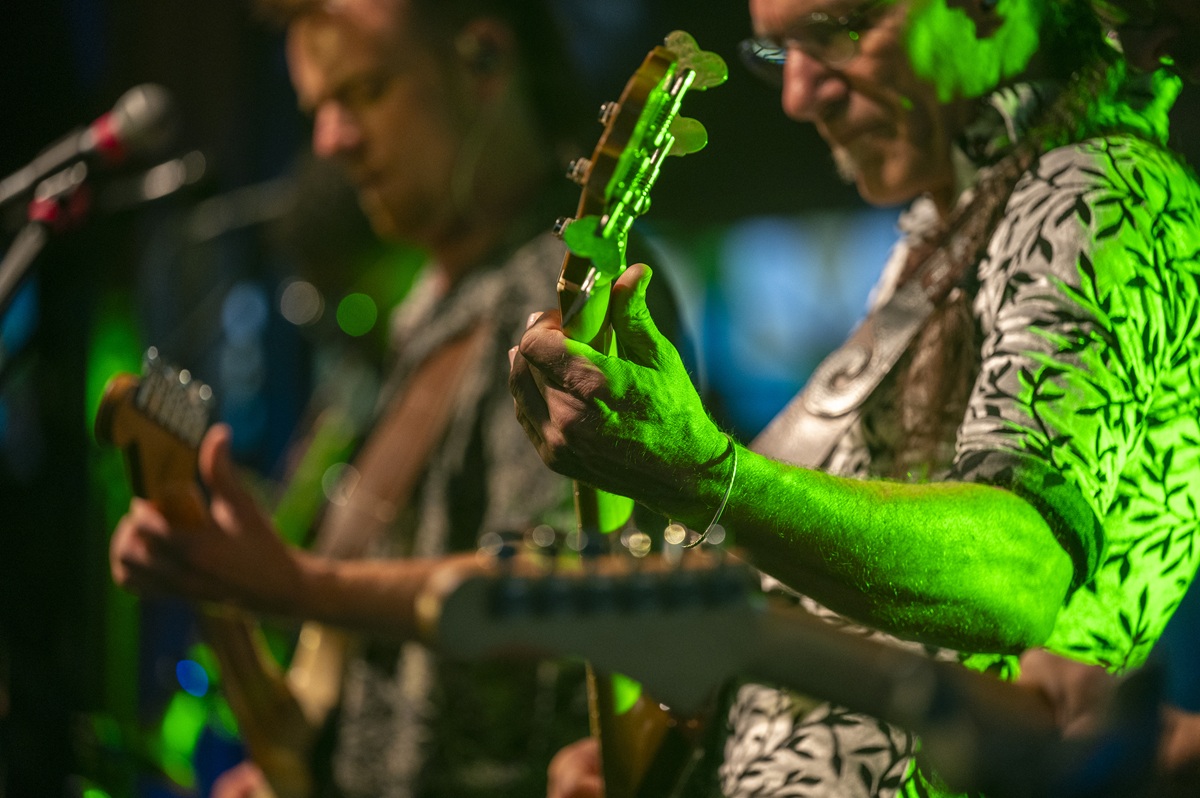 Zwei Gitarristen spielen gerade auf der Bühne und sind mit grünem Discolicht angeleuchtet.
