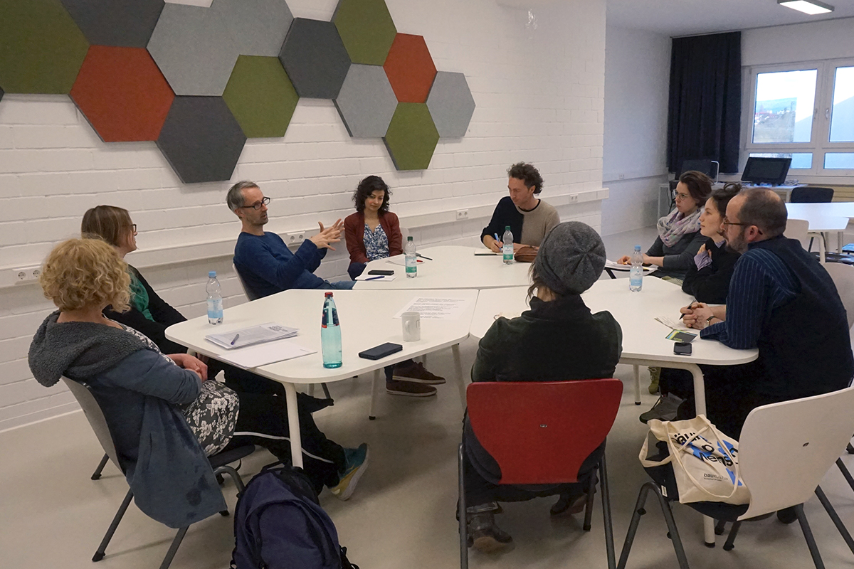 9 Menschen sitzen an einem Besprechungstisch