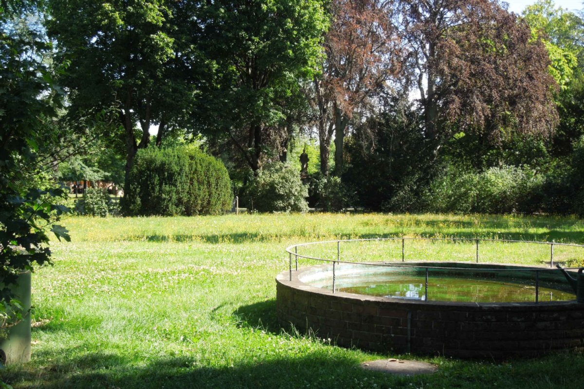 Wiese mit rundem Wasserbecken und Bäumen