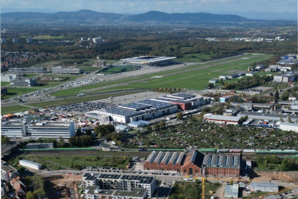 Luftbild mit Industriegebäuden und Grünflächen mit Bergkette im Hintergrund