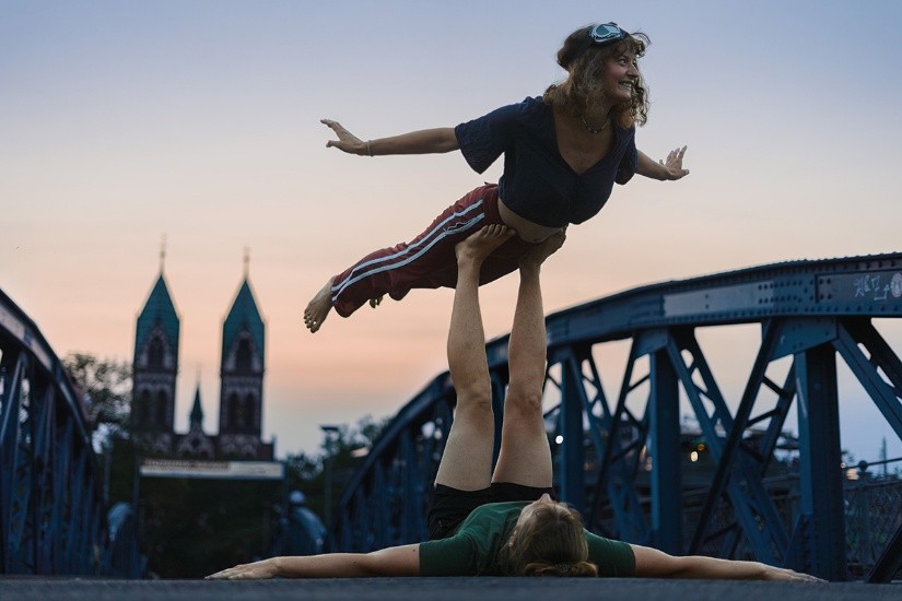 Foto: Amelie Nauen Person liegt mit nach oben gestreckten Beinen auf dem Rücken auf der Wiwillibrücke. Eine Person liegt auf den ausgestreckten Beinen und streckt sich wie ein Flugzeug.
