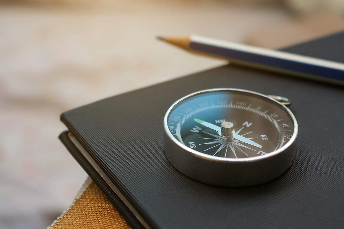 Auf einem schwarzen Notizbuch liegen ein Kompass und ein Bleistift