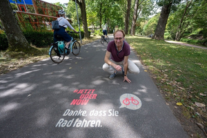 Baubürgermeister Haag kniet vor Graffiti-Spruch auf einem Radweg: Jetzt oder Now. Danke, dass Sie Rad fahren.