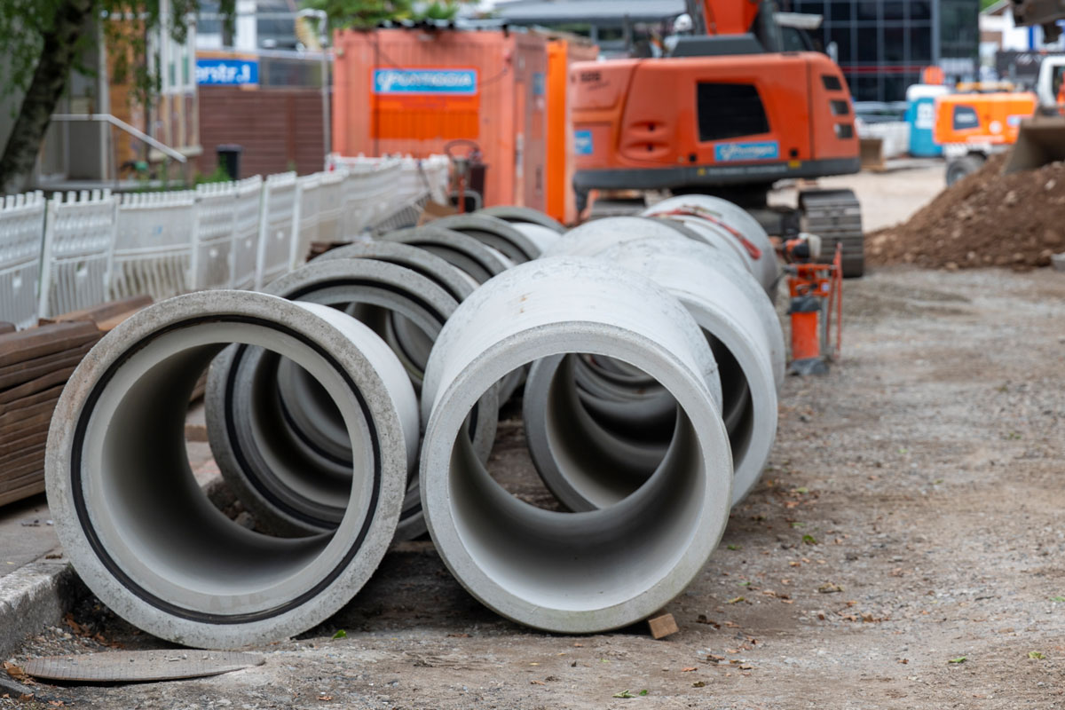 leere Kanalrohre liegen auf einer Baustelle, im Hintergrund ein Bagger