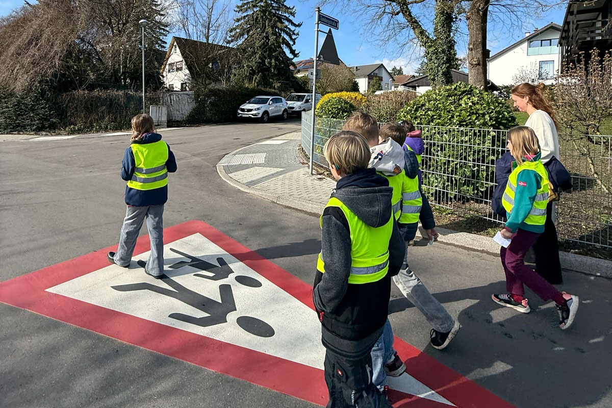 Schulkinder mit gelben Warnwesten auf einer verkhrsberuhigten Straße auf dem Weg zur Schule