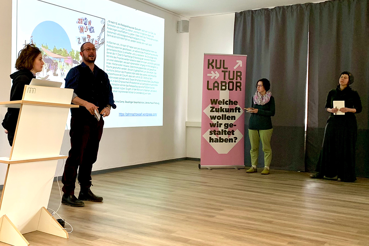 Vier Refernt_innen vor einem gebeamten Bild