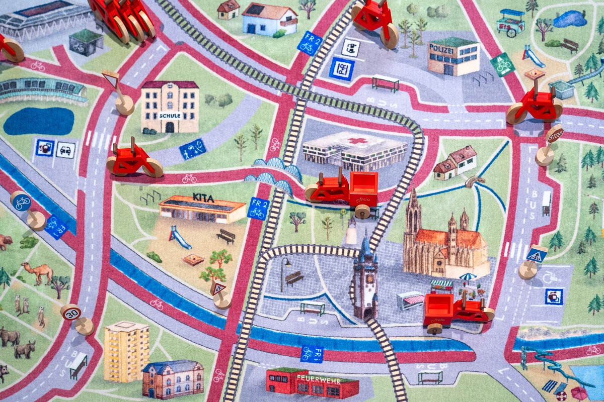 Freiburger Spielteppich, bedruckt mit Stadion, Münster und anderen Gebäuden, darauf kleine Spielfahrzeuge