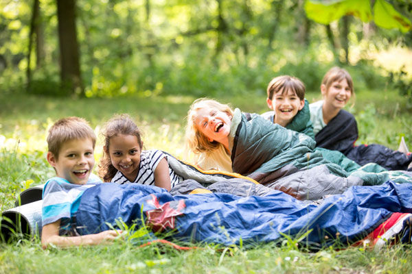Fünf fröhliche Kinder in Schlafsäcken auf einer Wiese