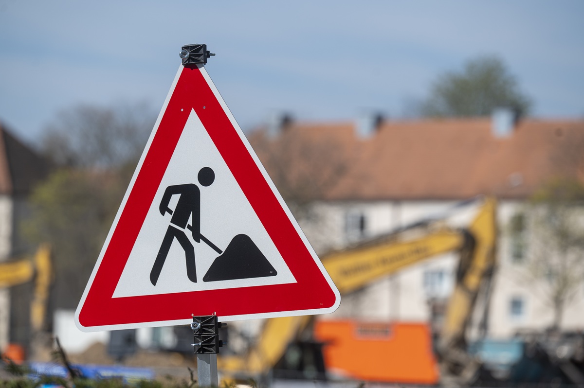 Baustellenschild, unscharf im Hintergrund stehen mehrere Bagger.