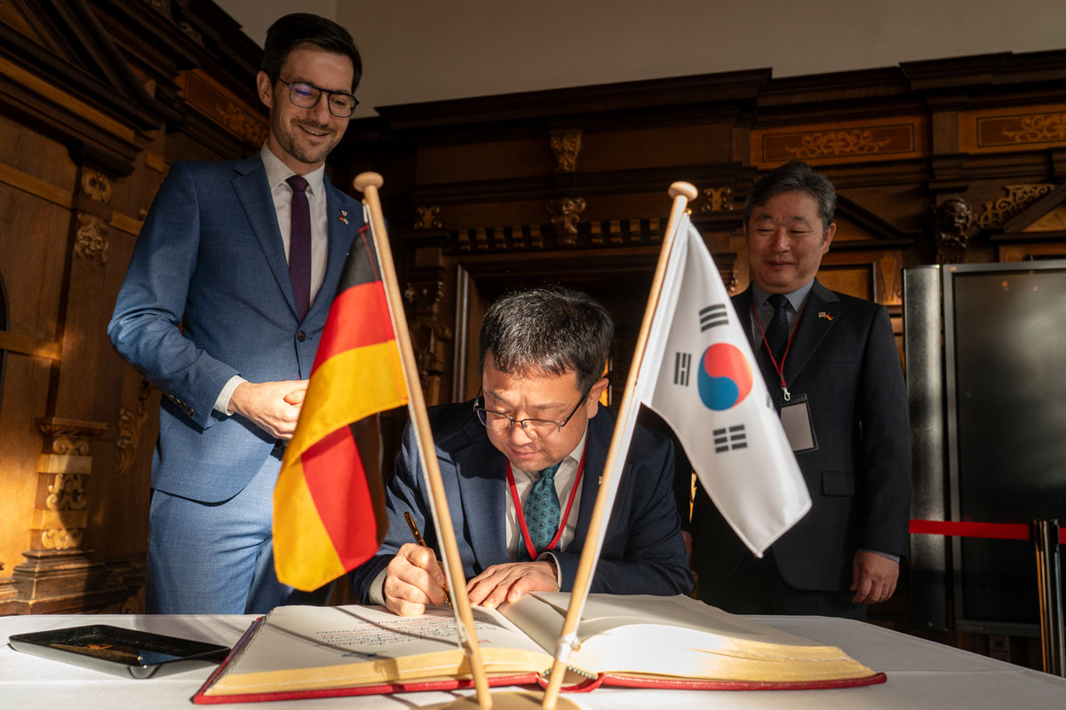 Drei Personen stehen vor einem Buch und schauen es an, unterschreiben darin