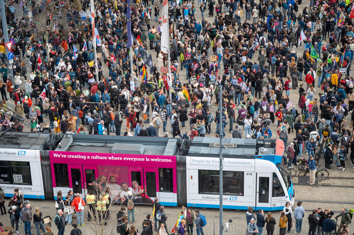 Große Menschenmenge (Demonstrationszug) wird geteilt durch eine Straßenbahn