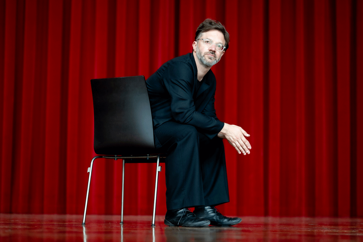 Mann sitzt auf einem Stuhl vor rotem Vorhang